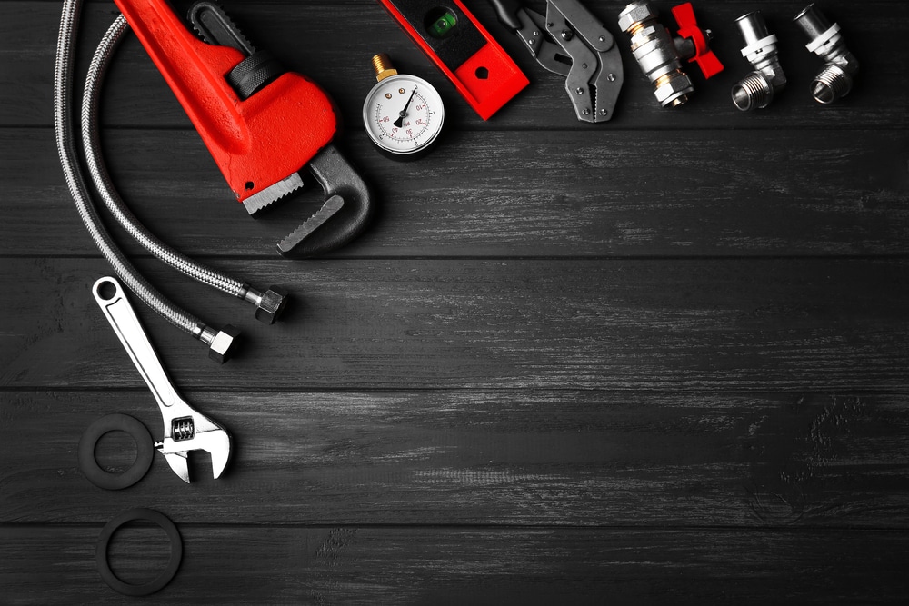 Common plumbing issues that arise during Calgary Winters portrayed by a semicircle of plumbing tools against a black wooden backdrop.